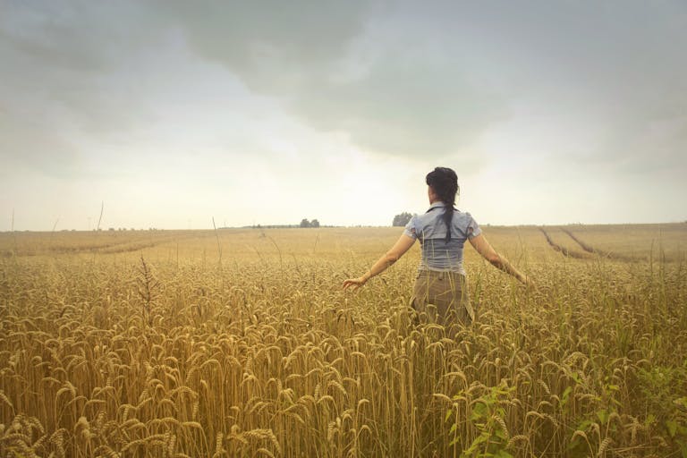 Woman walking through a peaceful wheat field, embracing rural nature and the open sky.